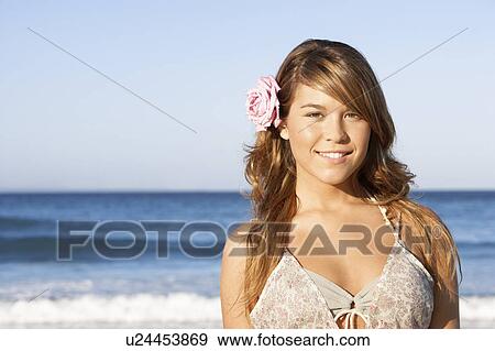 Young woman standing by sea with flower in hair, portrait View Large Photo Image Stock Photo - Young woman standing by sea with flower in hair, portrait. Fotosearch