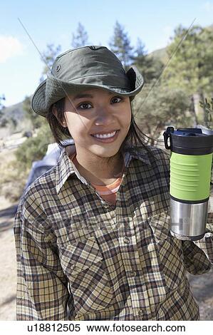 Stock Photography - Young woman standing outdoors, holding travel mug.. Fotosearch