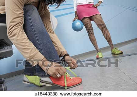 Stock Photo - Young woman tying bowling shoes, low section. Fotosearch