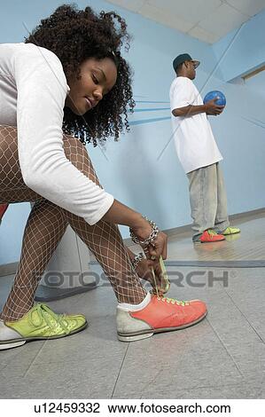Stock Image - Young woman tying bowling shoes, portrait. Fotosearch