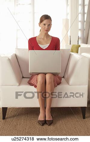 Stock Photo - Young woman using laptop in living room, portrait. Fotosearch