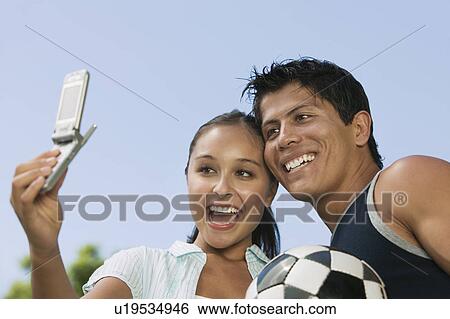 Young woman using mobile phone, photographing self with young man. View Large Photo Image Stock Photograph - Young woman using mobile phone, photographing self with young man.. Fotosearch