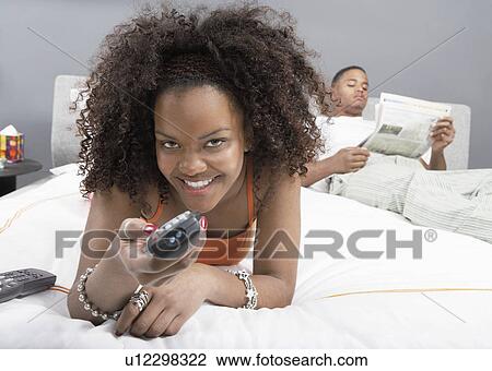 Young woman using remote control lying in bed next to boyfriend View Large Photo Image Stock Image - Young woman using remote control lying in bed next to boyfriend. Fotosearch