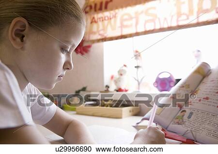 Stock Image - 10 year old girl sits at window desk doing her homework. Fotosearch