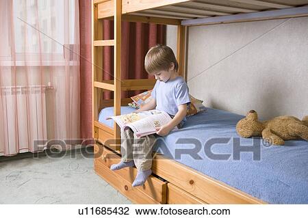 Stock Image - 5 year old boy sits on bunk bed reading a book. Fotosearch