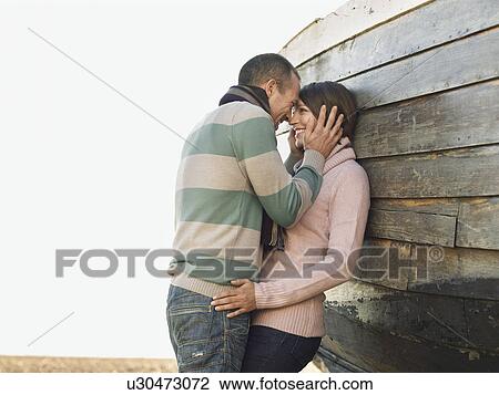 Affectionate couple leaning against wooden hull of boat on beach, side view View Large Photo Image Stock Image - Affectionate couple leaning against wooden hull of boat on beach, side view. Fotosearch