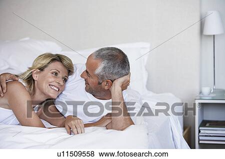 Stock Photo - Affectionate couple looking in each others eyes, lying in bed. Fotosearch