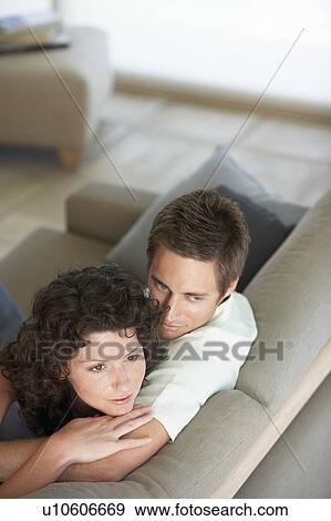 Stock Photo - Affectionate couple sitting on couch in living room, elevated view. Fotosearch