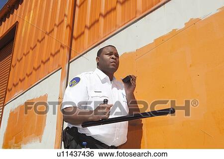 Stock Photograph - Armed security guard investigates warehouse exterior. Fotosearch