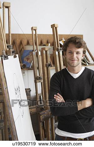 Stock Photo - Artist standing by charcoal portrait in studio, smiling. Fotosearch