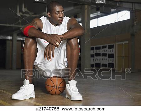 Stock Photo - Basketball player sitting on ball, portrait. Fotosearch