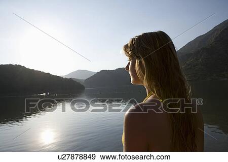Stock Photo - Blonde woman looks out across morning sunrise over lake. Fotosearch