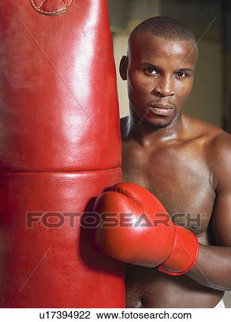 Stock Image - Boxer holding punching bag, portrait. Fotosearch