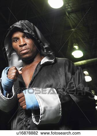 Stock Image - Boxer wearing robe with hood up, clenching fists, portrait. Fotosearch