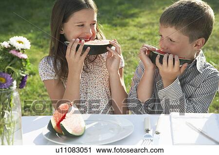 Boy and girl (7-9) sitting at table in garden and eating watermelon View Large Photo Image Stock Image - Boy and girl (7-9) sitting at table in garden and eating watermelon. Fotosearch