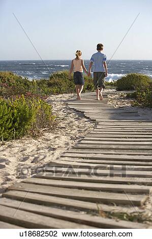 Boy and girl walking hand in hand, along boardwalk toward sea, back view View Large Photo Image Stock Image - Boy and girl walking hand in hand, along boardwalk toward sea, back view. Fotosearch