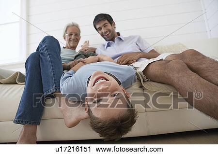 Stock Image - Boy hanging upside down off couch, with father and grandfather sitting beside him. Fotosearch