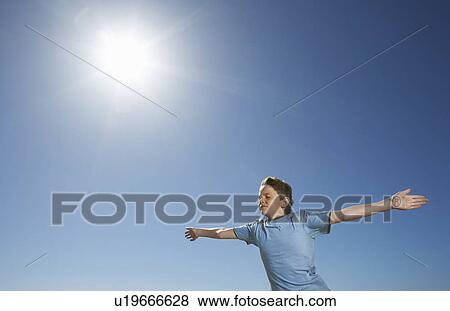 Stock Photo - Boy with arms outstretched, half length, in front of blue sky. Fotosearch