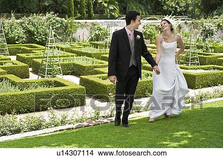Bride and groom walking hand in hand in garden View Large Photo Image Picture - Bride and groom walking hand in hand in garden. Fotosearch