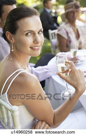 Bride sitting at wedding table, holding wineglass, smiling View Large Photo Image Stock Photo - Bride sitting at wedding table, holding wineglass, smiling. Fotosearch