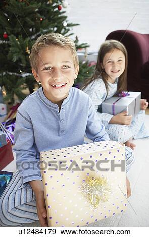 Brother and sister holding gifts sitting by christmas tree, portrait View Large Photo Image Stock Photo - Brother and sister holding gifts sitting by christmas tree, portrait. Fotosearch