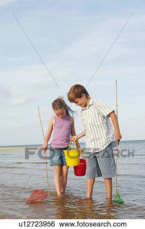Stock Photograph - Brother and Sister in surf on beach with buckets and small fishnets. Fotosearch