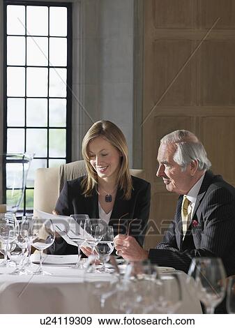 Stock Photo - Business man and woman sitting at restaurant table reading documents. Fotosearch