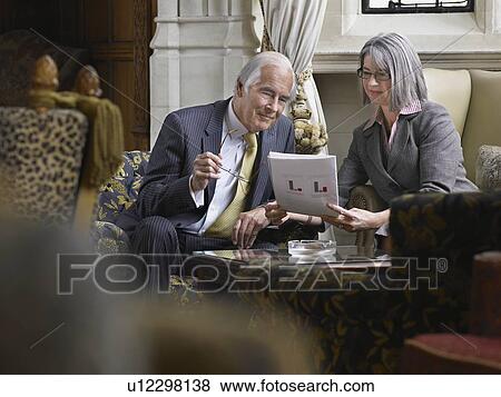 Stock Photo - Business man and woman sitting indoors looking at documents. Fotosearch