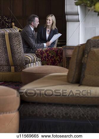 Stock Photography - Business man and woman talking in lobby, sofas in foreground. Fotosearch