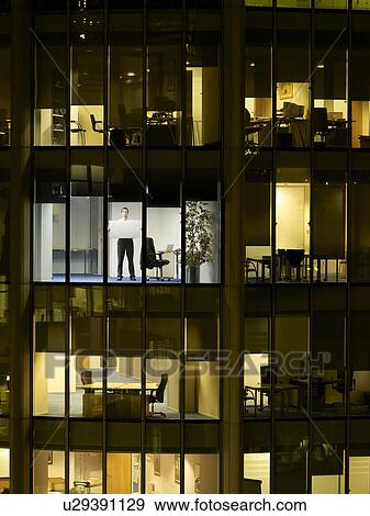 Stock Photo - Business man holding up blank paper in office, view from building exterior. Fotosearch
