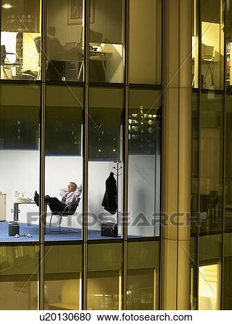Business man relaxing in office, view from building exterior View Large Photo Image Stock Image - Business man relaxing in office, view from building exterior. Fotosearch