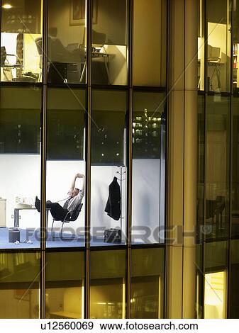 Stock Photo - Business man relaxing in office, view from building exterior. Fotosearch