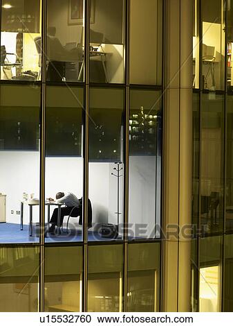 Business man resting at desk in office, view from building exterior View Large Photo Image Stock Image - Business man resting at desk in office, view from building exterior. Fotosearch
