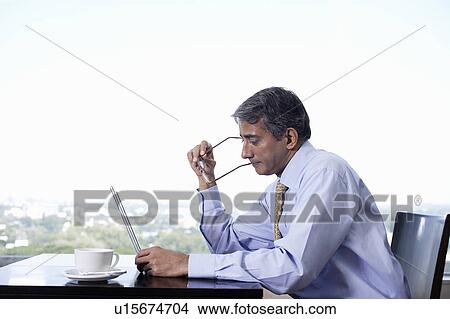 Business man sitting at table, using laptop View Large Photo Image Picture - Business man sitting at table, using laptop. Fotosearch