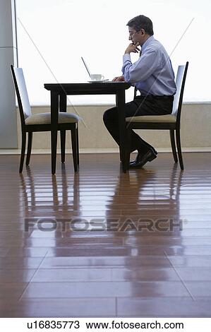 Business man sitting at table, using laptop View Large Photo Image Stock Image - Business man sitting at table, using laptop. Fotosearch