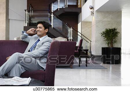 Business man sitting on sofa, using cell phone View Large Photo Image Stock Photography - Business man sitting on sofa, using cell phone. Fotosearch