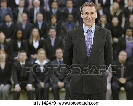 Stock Photo - Business man standing in front of business people sitting on tribune, portrait. Fotosearch