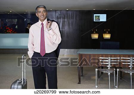 Stock Photo - Business man standing in hotel lobby, portrait. Fotosearch