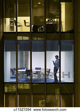 Picture - Business man text messaging in office, view from building exterior. Fotosearch