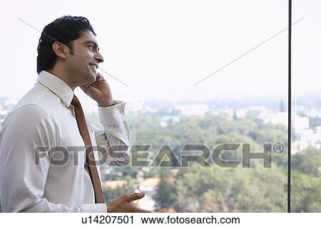 Stock Image - Business man using cell phone, smiling, side view. Fotosearch