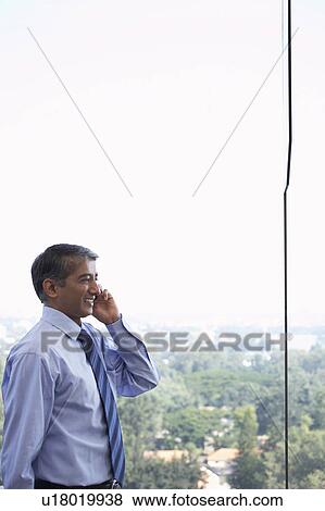 Business man using cell phone, smiling, side view View Large Photo Image Stock Photo - Business man using cell phone, smiling, side view. Fotosearch