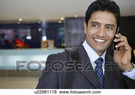 Stock Photo - Business man using mobile phone in hotel lobby. Fotosearch