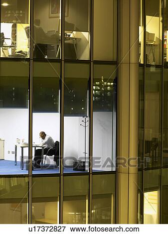 Business man working at desk in office, view from building exterior View Large Photo Image Stock Photo - Business man working at desk in office, view from building exterior. Fotosearch