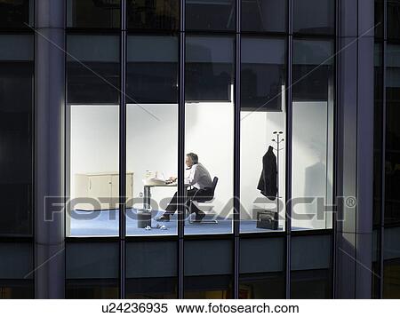 Stock Photography - Business man working at desk in office, view from building exterior. Fotosearch