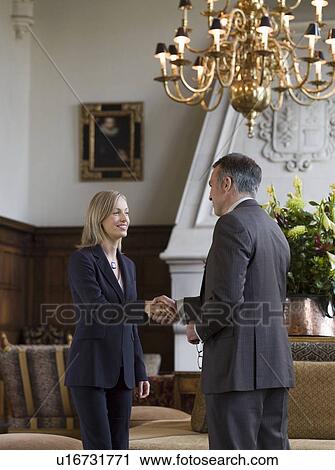 Stock Image - Business woman and man shaking hands under chandelier. Fotosearch
