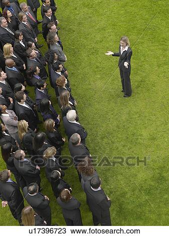 Stock Image - Business woman facing large group of business people in formation, elevated view. Fotosearch