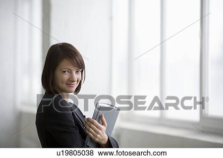Stock Photo - Business woman on holding file at warehouse windows. Fotosearch