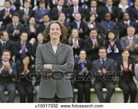 Stock Image - Business woman standing in front of business people sitting in bleachers, clapping, portrait. Fotosearch