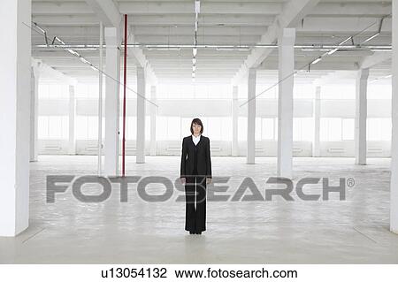 Stock Image - Business woman stands in empty warehouse. Fotosearch