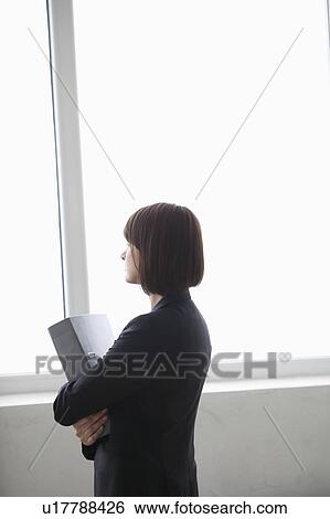 Business woman stands with file looking out of window View Large Photo Image Stock Photograph - Business woman stands with file looking out of window. Fotosearch